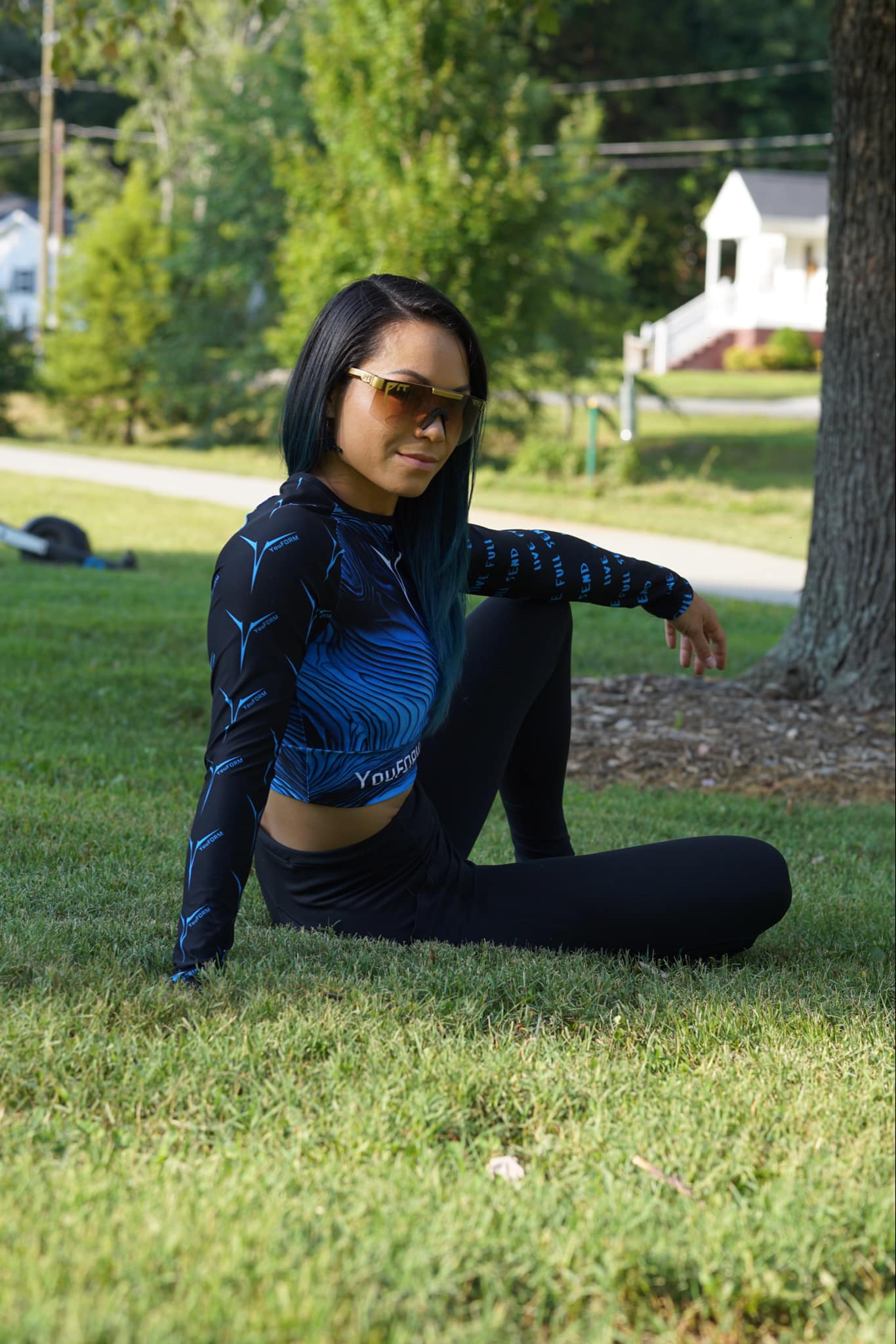 IMAGE OF KAY LOVE SITTING ON THE GROUND WEARING THE YOUFORM PADS CROPPED WOMEN'S RACE JERSEY AND BLACK PANTS WITH THE OUTDOORS BEHIND HER